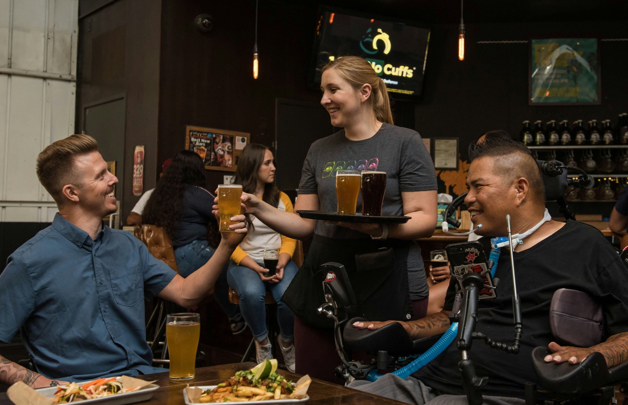 A group of people at a bar, including a wheelchair user being served by bartending staff